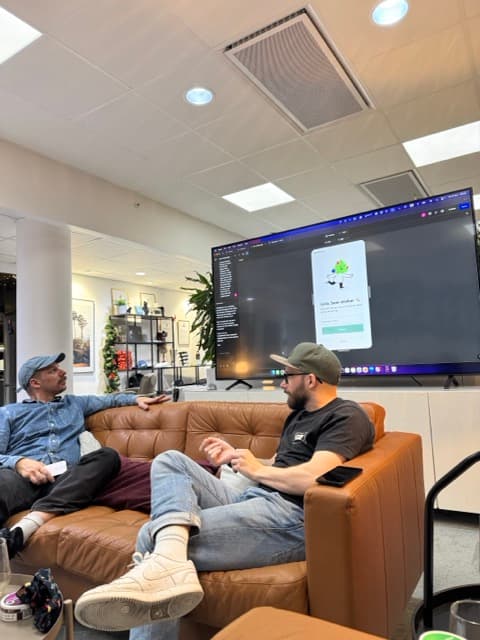 Two colleagues at the office in front of a screen showing the app being built in Figma Make